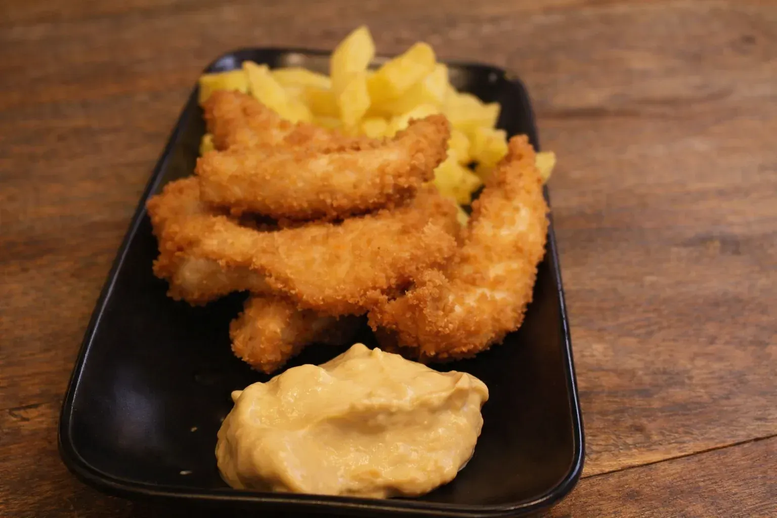 Fried shrimp and fries on a black plate with a side of dipping sauce