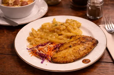 Un plato de pescado a la parrilla, rodajas de patata sazonadas y una pequeña guarnición de ensalada de col.