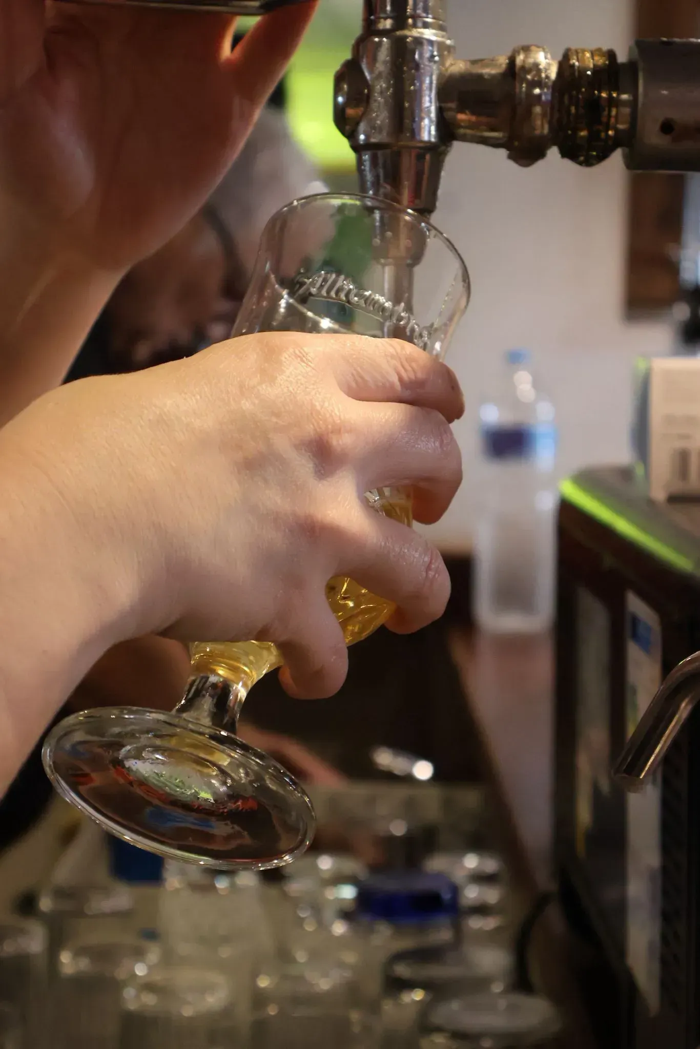 Una mano vierte cerveza dorada desde un grifo metálico en un vaso en un bar.