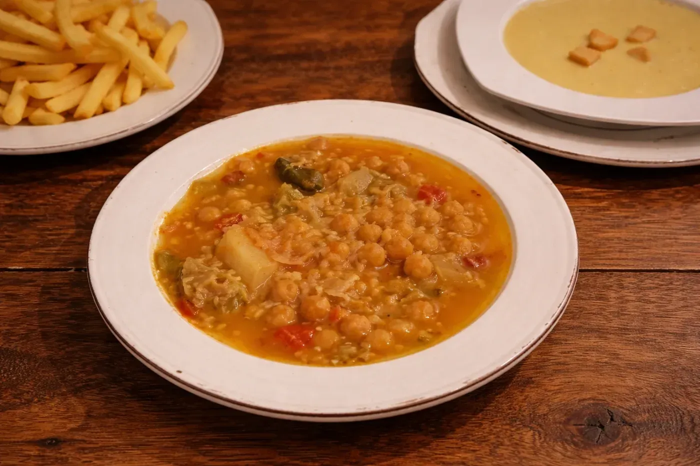 Bowls of soup, fries, and a creamy sauce on a wooden table
