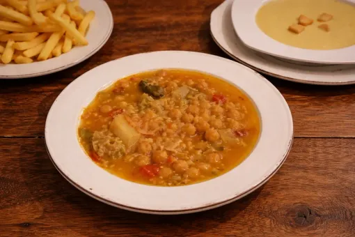 Un plato de estofado de garbanzos servido con una guarnición de patatas fritas y un pequeño tazón.