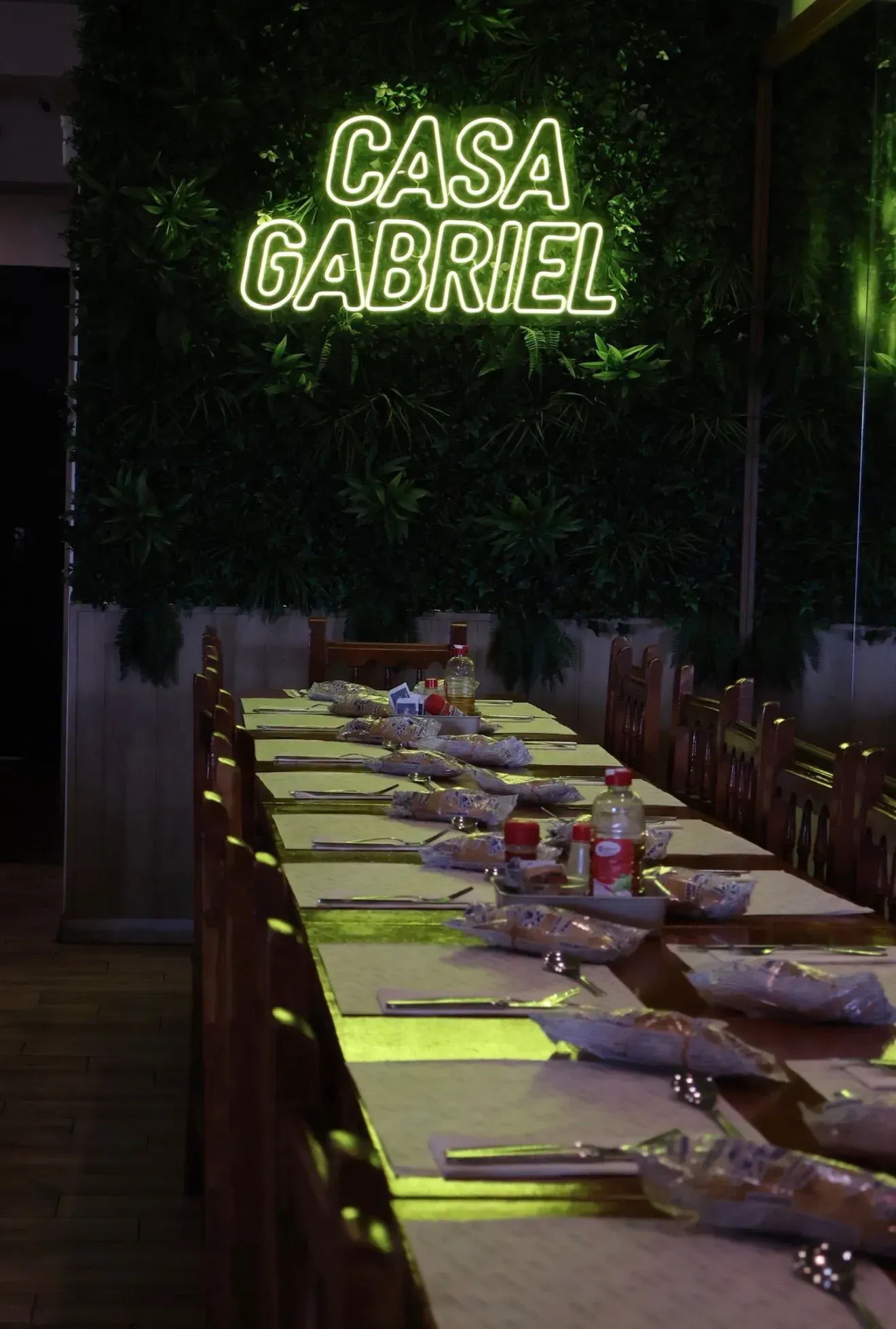 Letrero de neón “CASA GABRIEL” sobre una larga mesa de comedor puesta por la noche.
