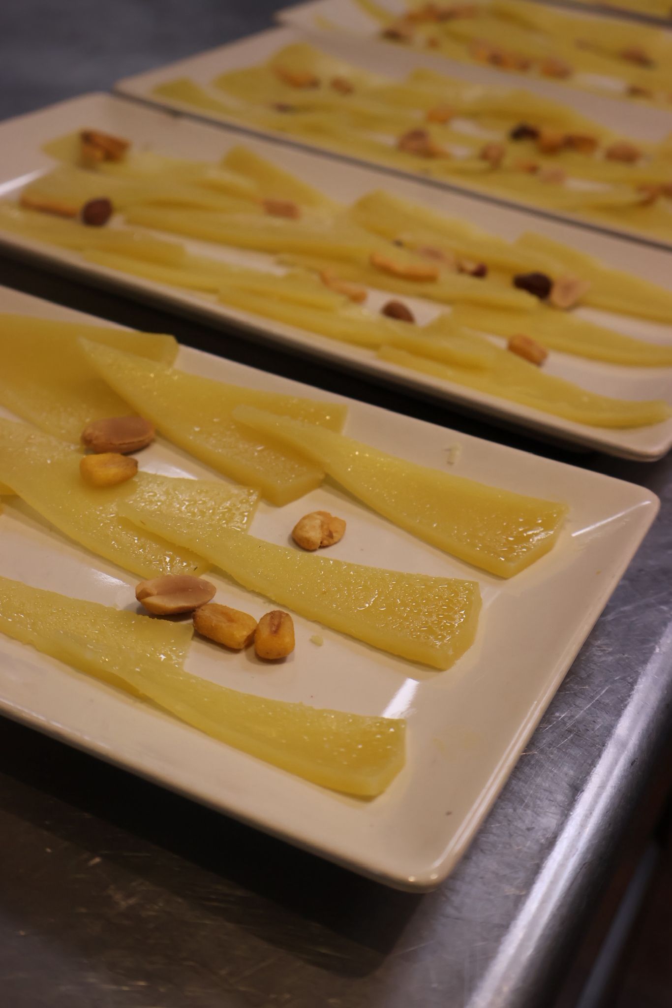 Platos con tiras de postre de color amarillo pálido cubiertas con nueces picadas sobre una mesa.
