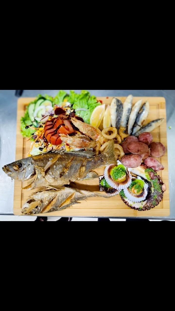 Una tabla de cortar de madera cubierta con pescado y verduras.