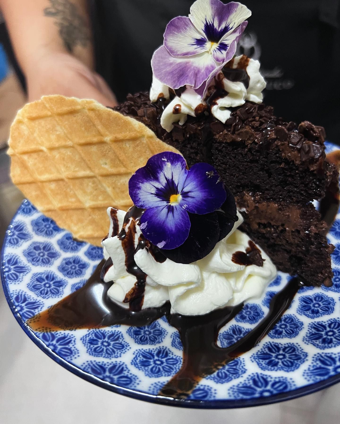 Un trozo de pastel de chocolate con crema batida y flores moradas encima.