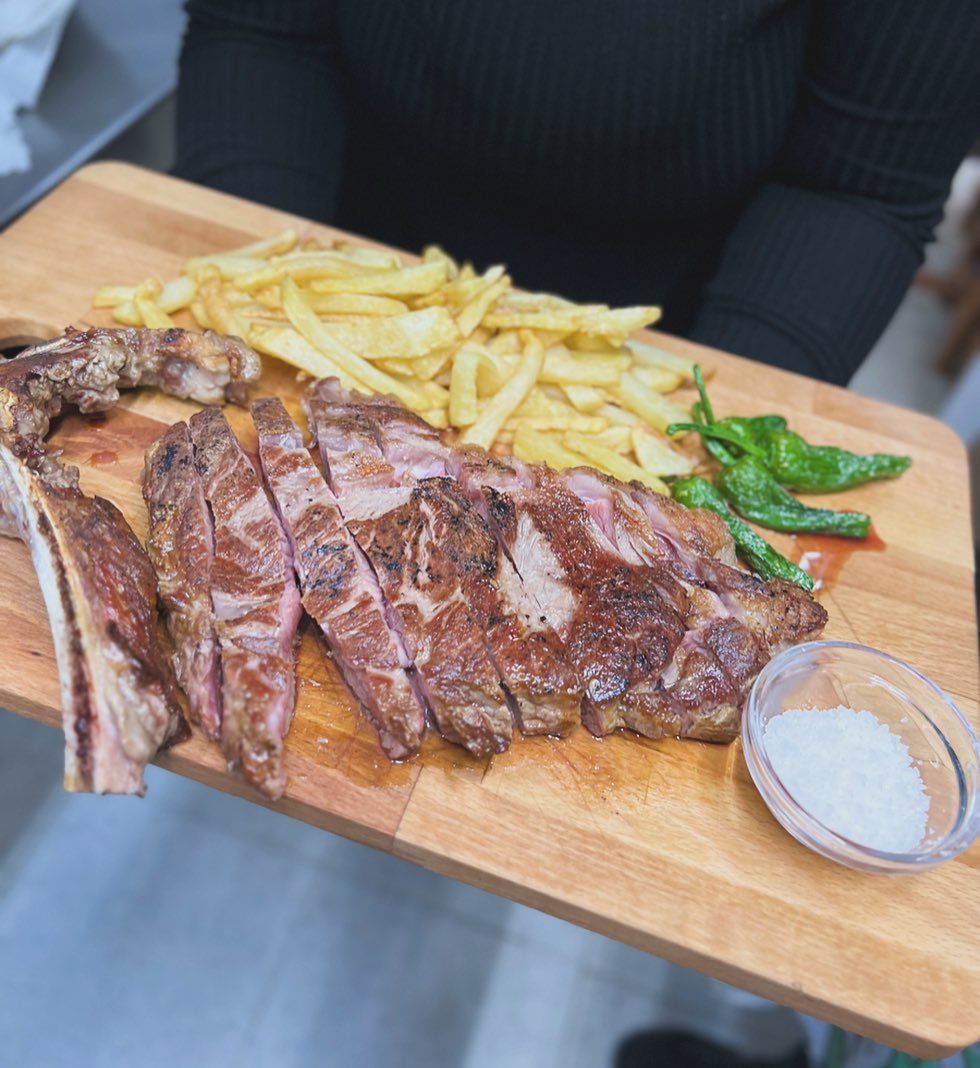 Una persona sostiene una tabla de cortar con carne y papas fritas encima.
