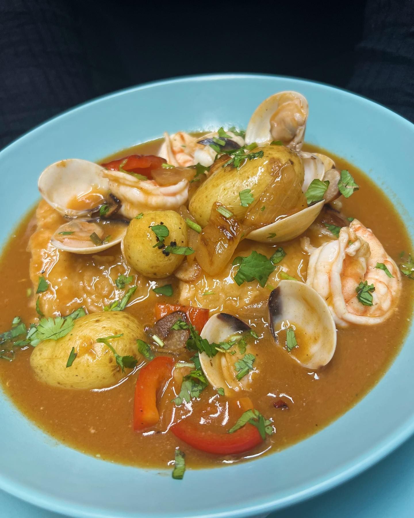 Un plato azul cubierto con un guiso de almejas y patatas.