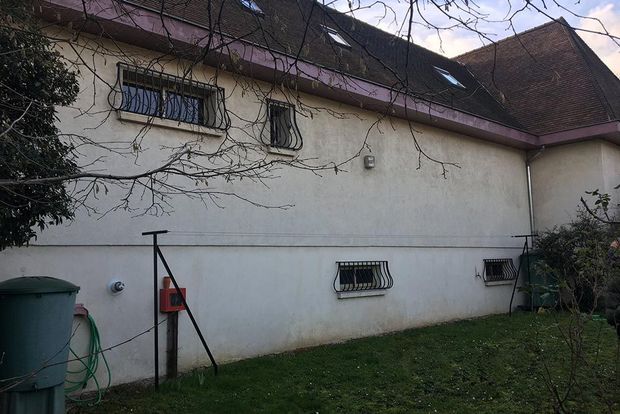 Extérieur d’une maison aux murs blancs en stuc, avec de petites fenêtres à barreaux et un toit de tuiles rouges