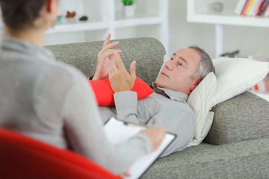 Terapeuta hablando con un paciente acostado en un sofá durante una sesión de terapia.
