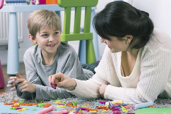 Una mujer y un niño juegan con cuentas de colores en el suelo, sonriendo y hablando juntos.