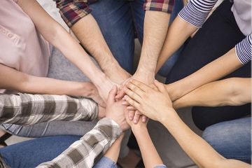 Varias personas juntan las manos en un círculo de equipo.