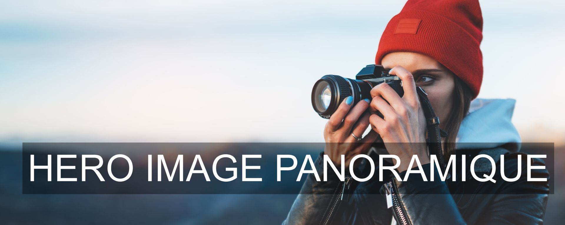 Image panoramique d'un plan serré d'une femme de profil coiffée d'un bonnet rouge qui prend une photographie d'un sujet hors-champ