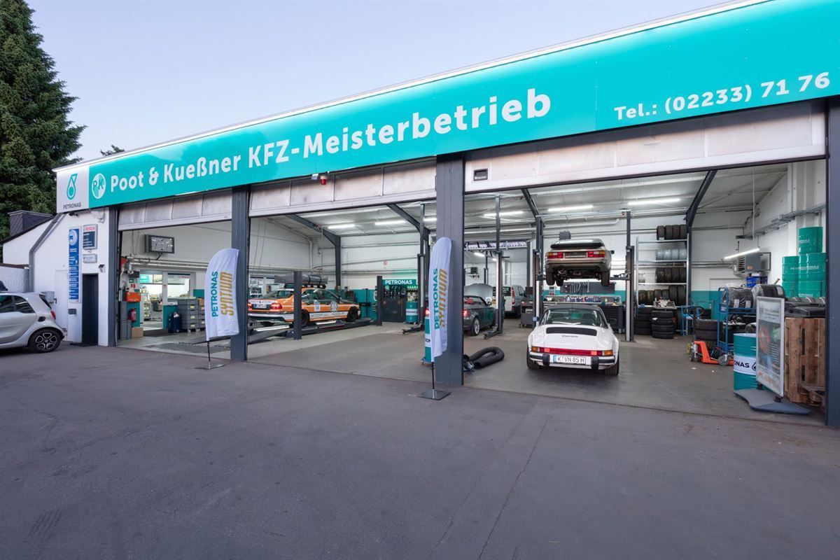 Ein weißes Auto steht vor einem Gebäude mit der Aufschrift „Meisterbetrieb“
