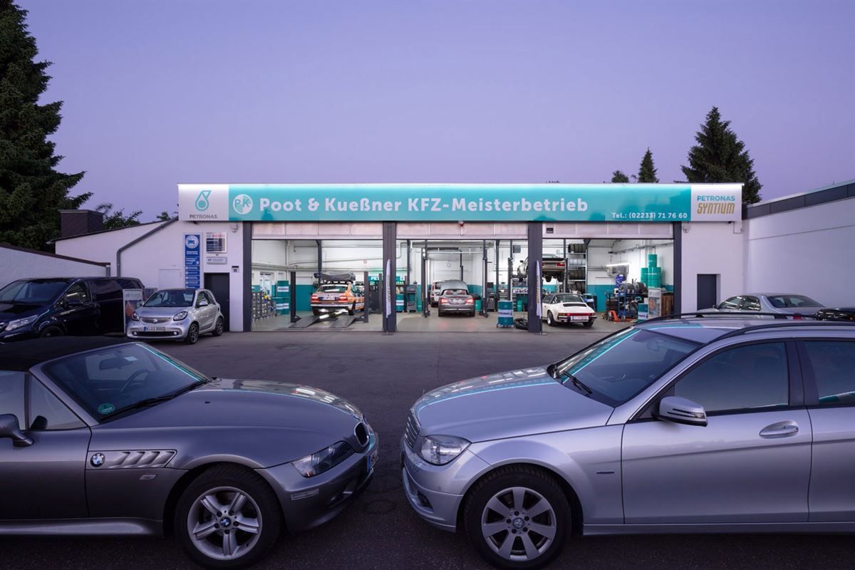 Zwei silberne Autos stehen vor einer Garage mit einem Schild mit der Aufschrift 