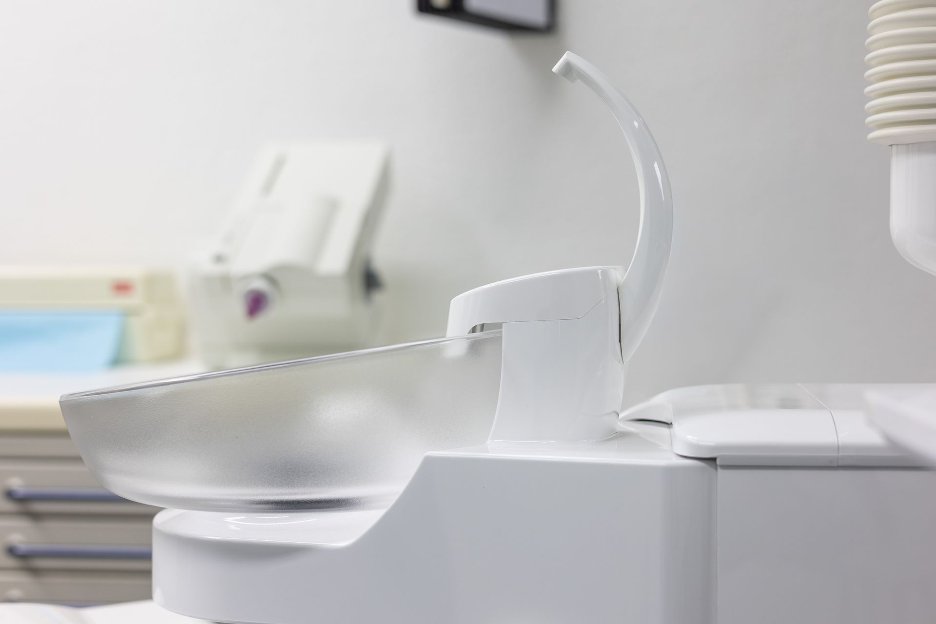 Spucknapf auf einem Zahnarztstuhl in einer hellen, weißen Zahnarztpraxis.