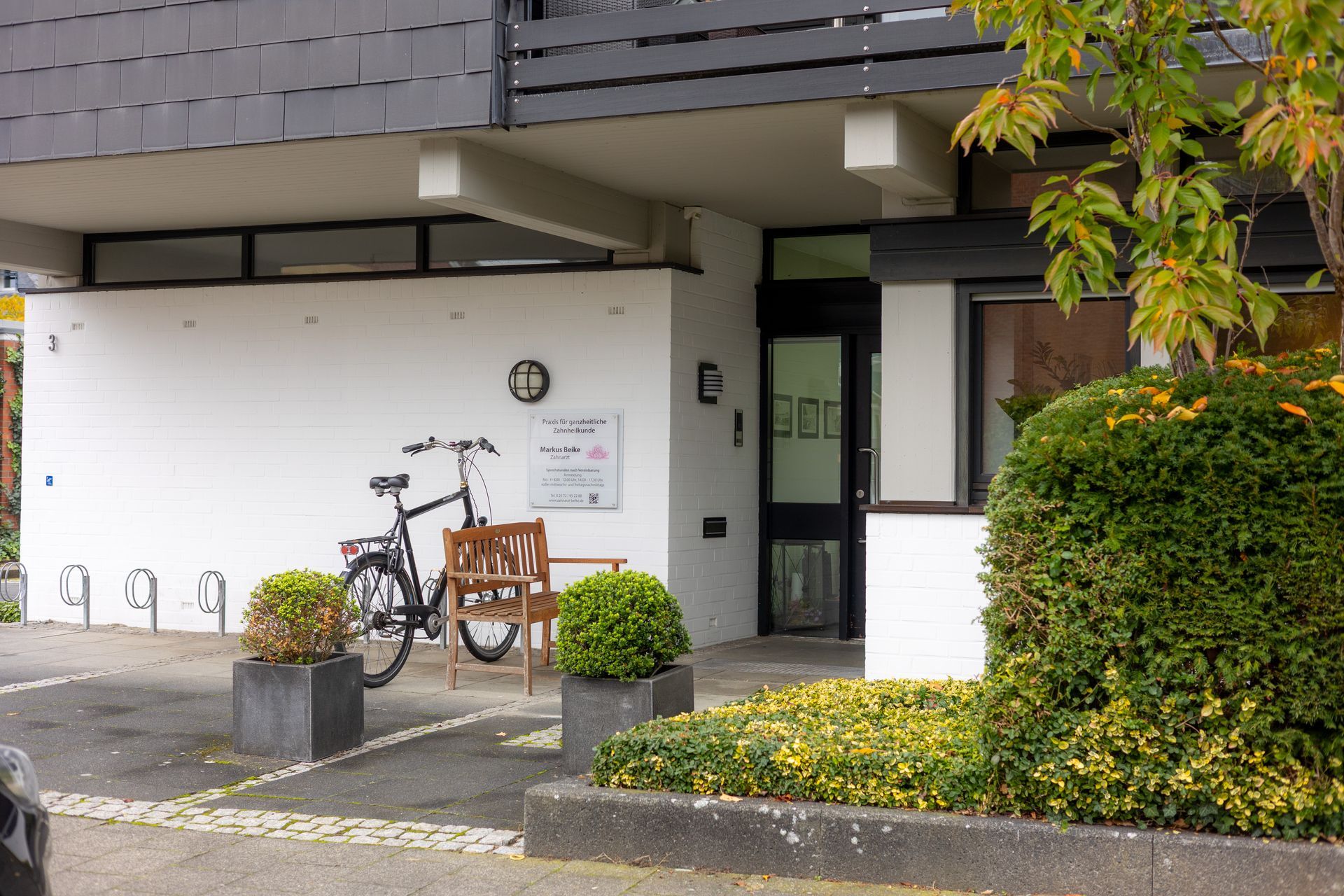 Außenansicht eines weißen Gebäudes mit einer schwarzen Tür, einem Fahrrad und Landschaftsgestaltung.