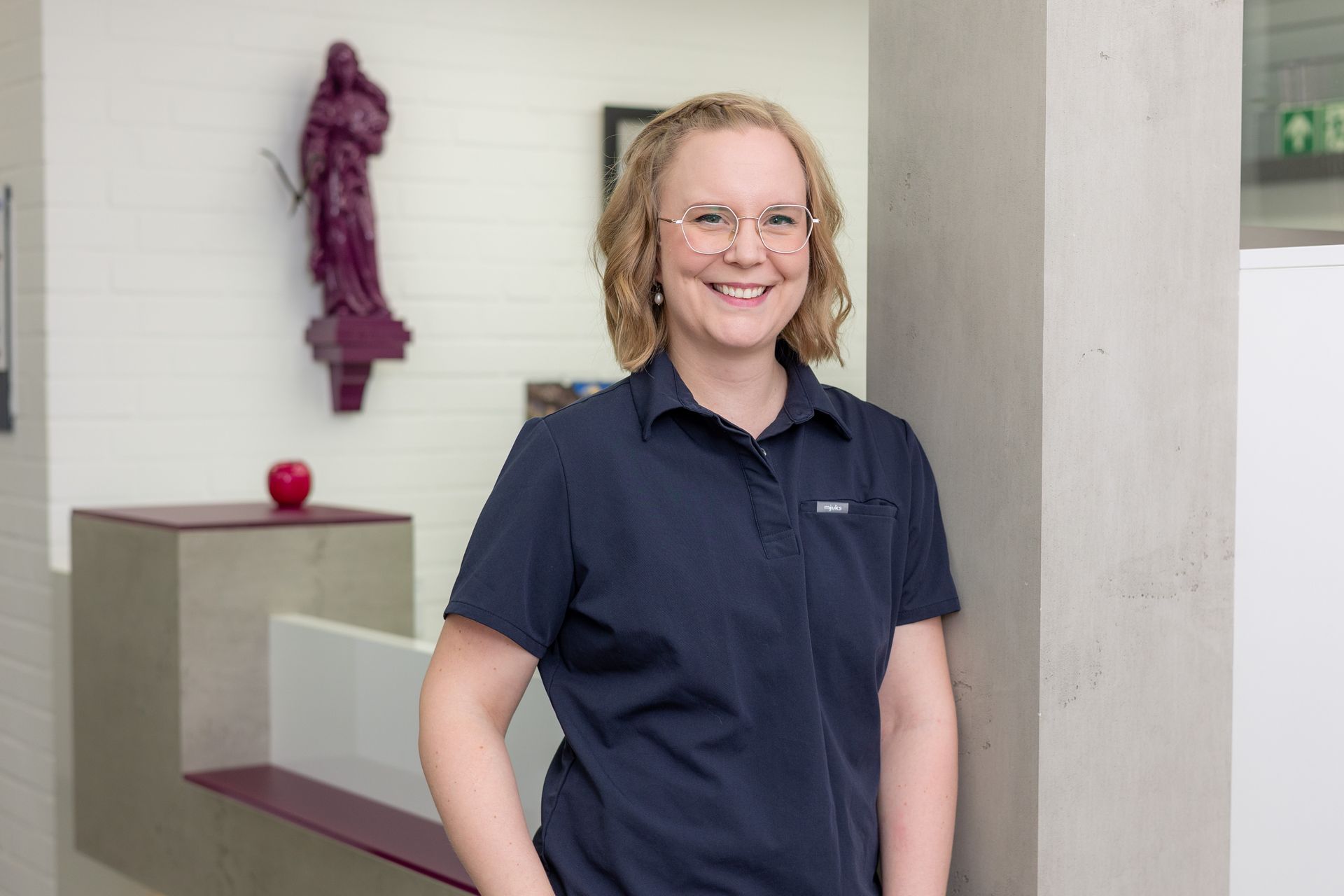 Frau mit Brille und marineblauem Hemd lächelt in einer Büroumgebung in die Kamera.