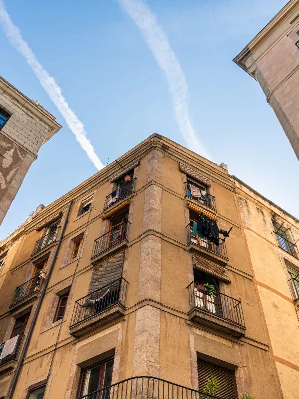 Vista desde un ángulo bajo de un edificio de apartamentos color canela con balcones contra un cielo azul