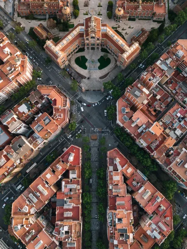 Vista aérea de una intersección de cuatro vías rodeada de edificios con tejados rojos y una pequeña plaza central.
