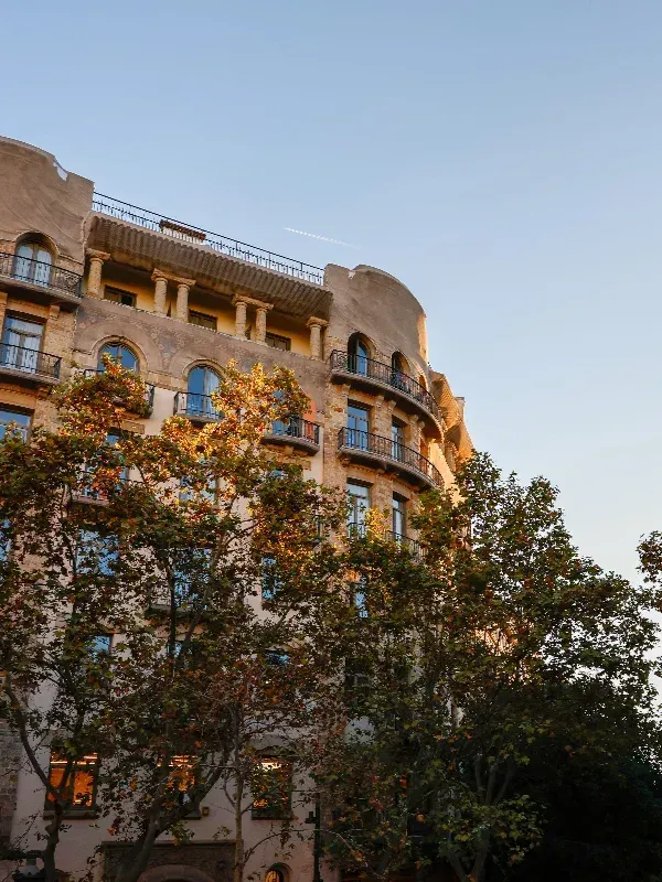 Edificio de apartamentos color canela bañado por el sol, con ventanas arqueadas y árboles en la fachada.