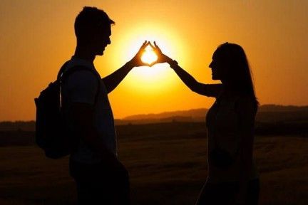 Couple en silhouette formant un cœur avec leurs mains au coucher du soleil dans un champ ouvert