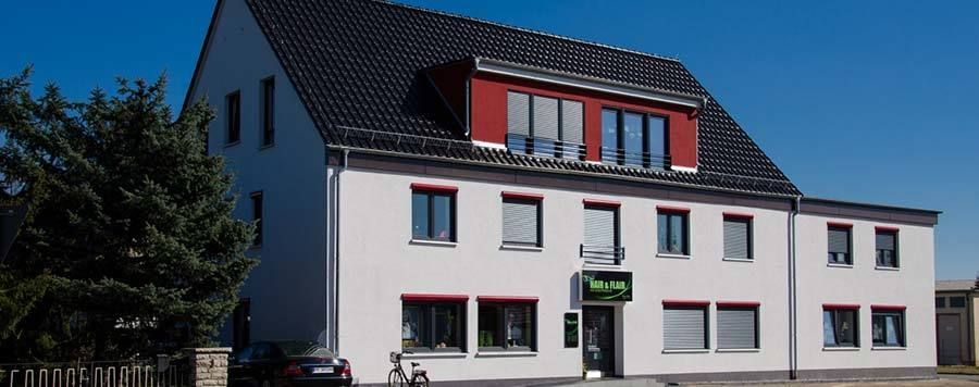 Ein weißes Haus, mit einem dunklen Dach und roter Fassade um die oberen Fenster