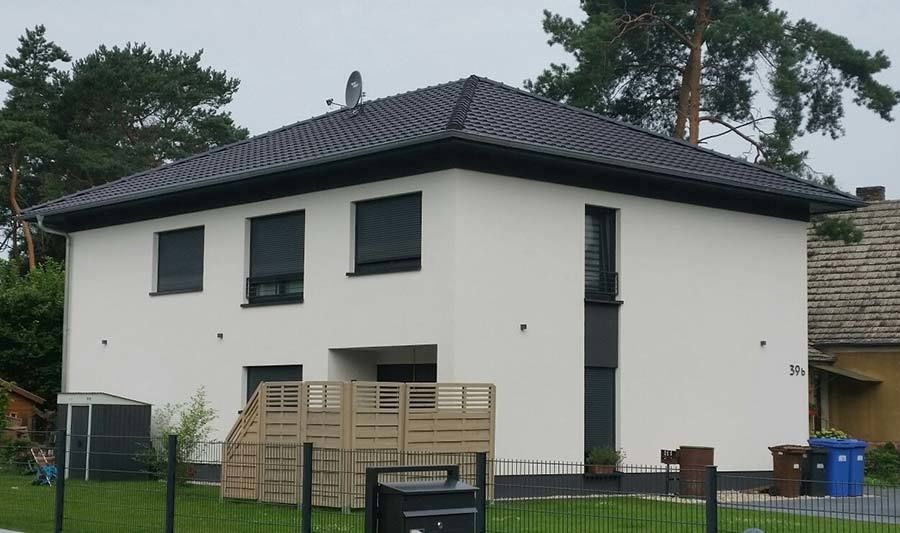 Ein weißes Haus mit dunklem Dach und einem Zaun. (Nachher)