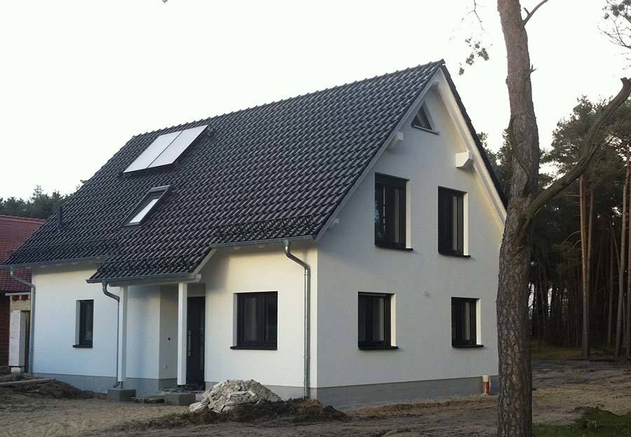 Ein weißes Haus mit dunklem Dach. Vorgarten ist noch unfertig (Vorher)