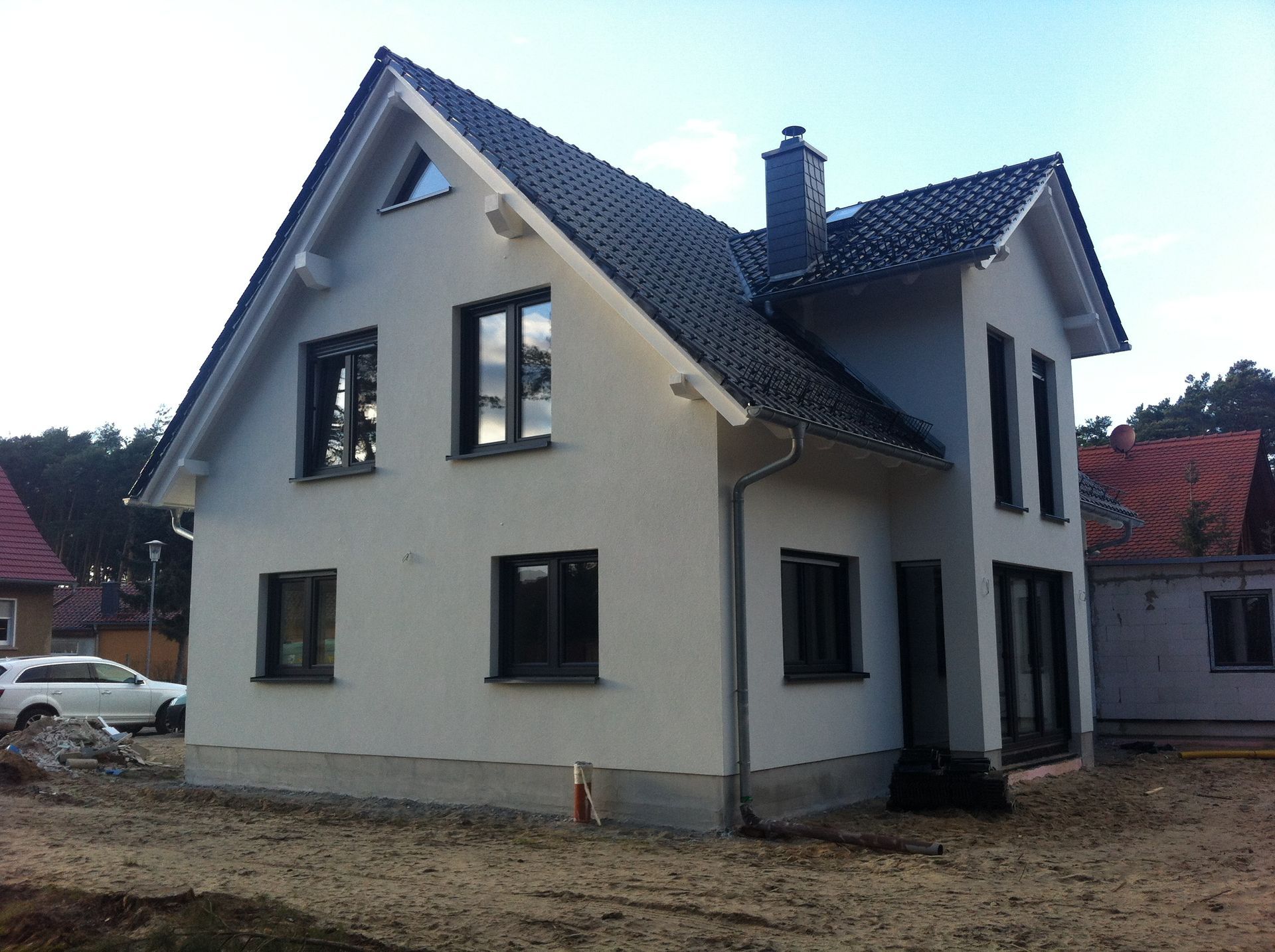 Ein weißes Haus mit dunklem Dach. Vorgarten ist noch unfertig (Vorher)