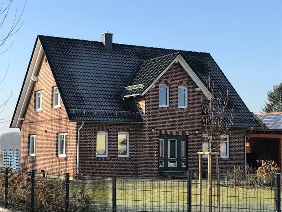 Ein großes Backsteinhaus mit schwarzem Dach und einem Zaun davor.