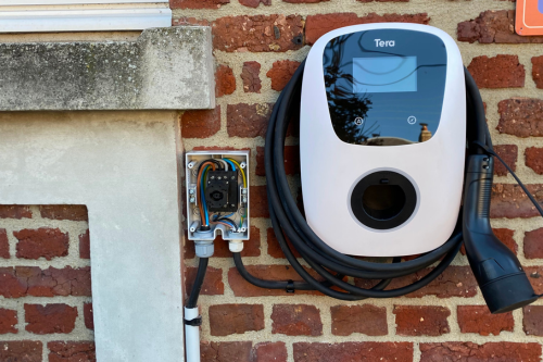 Un chargeur de voiture électrique blanc est fixé à un mur de briques.