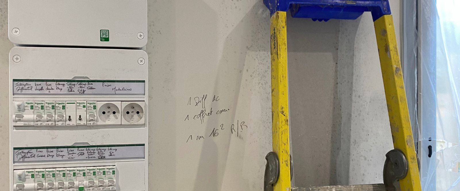Une échelle jaune est posée à côté d'une boîte blanche sur un mur.