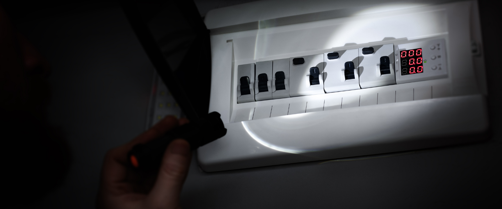 Une personne utilise une lampe de poche pour vérifier une boîte à fusibles.