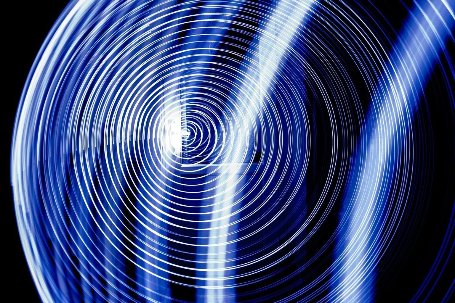 Círculos azules concéntricos y rayas de luz sobre un fondo negro, creando un efecto de remolino.