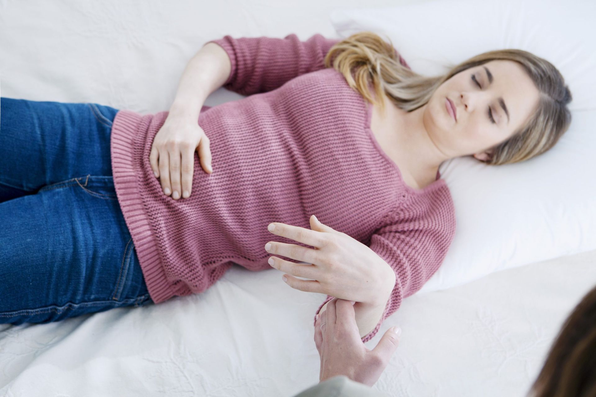 Una persona yace sobre una superficie blanca, aparentemente recibiendo una toma de pulso de un profesional sanitario en el brazo.