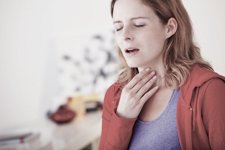 Mujer con ojos cerrados, chaqueta roja, tocándose la garganta, parece tener dolor de garganta.