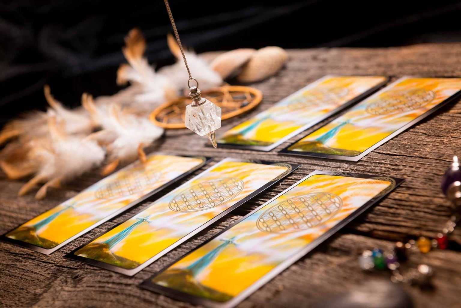Péndulo sobre cartas del tarot sobre una mesa de madera con plumas, conchas y cristales.