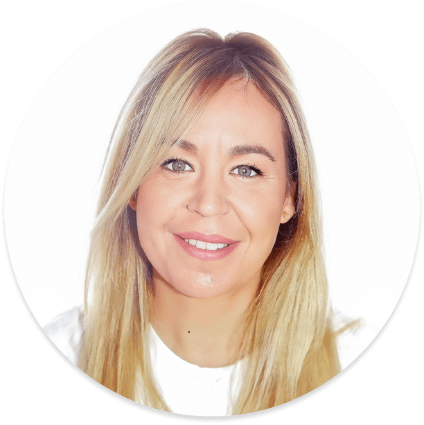 Mujer rubia sonriendo, vistiendo una camisa blanca, sobre un fondo blanco.