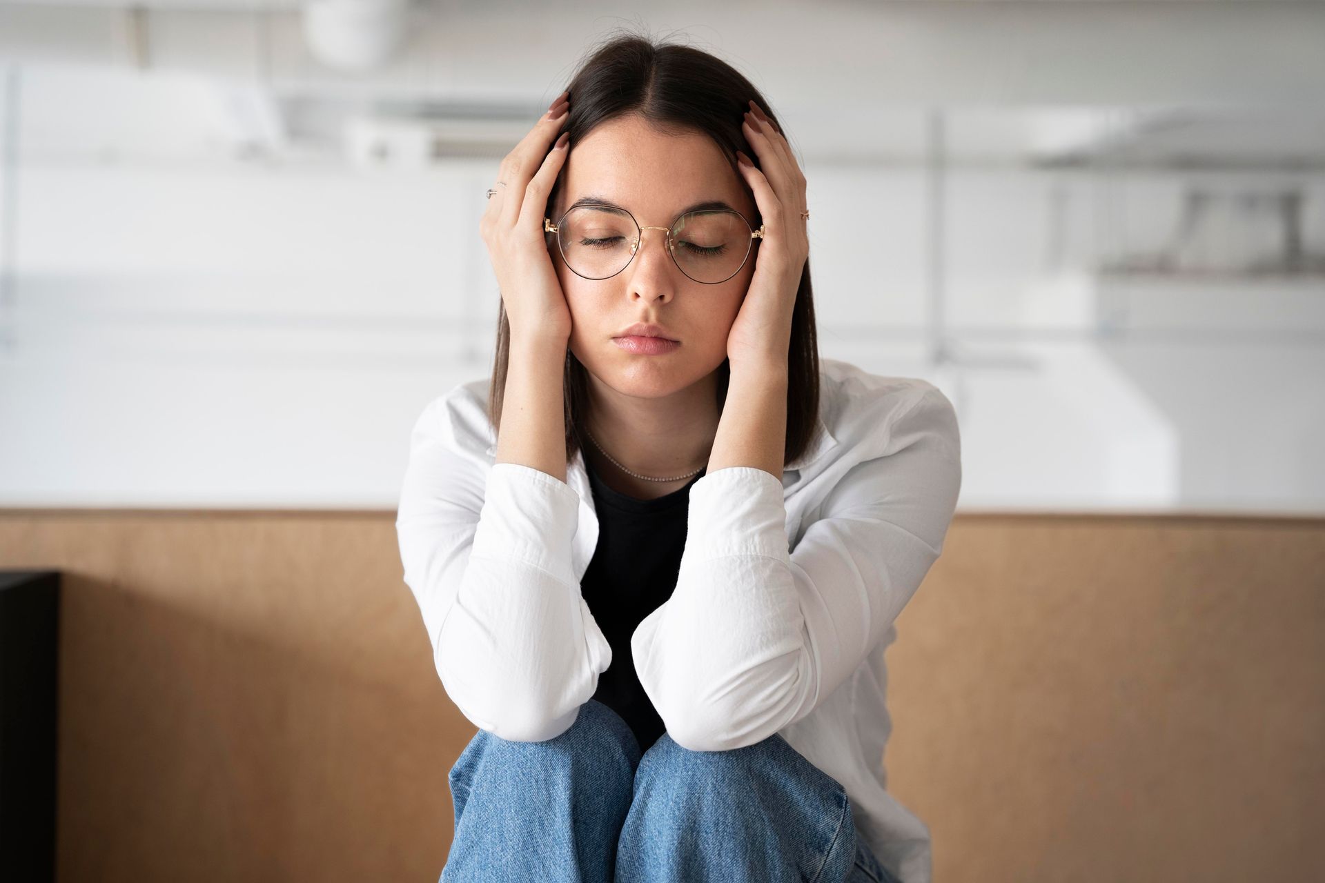 Mujer con cabello rizado, sujetándose las sienes, mirando hacia abajo con expresión angustiada.