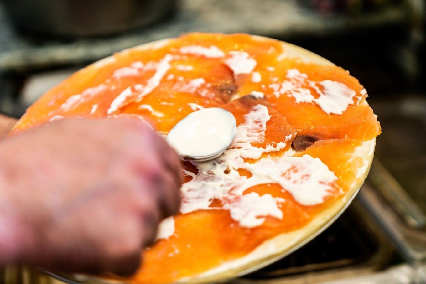 Photo d'une pizza au saumon, en train d'être badigeonnée de crème