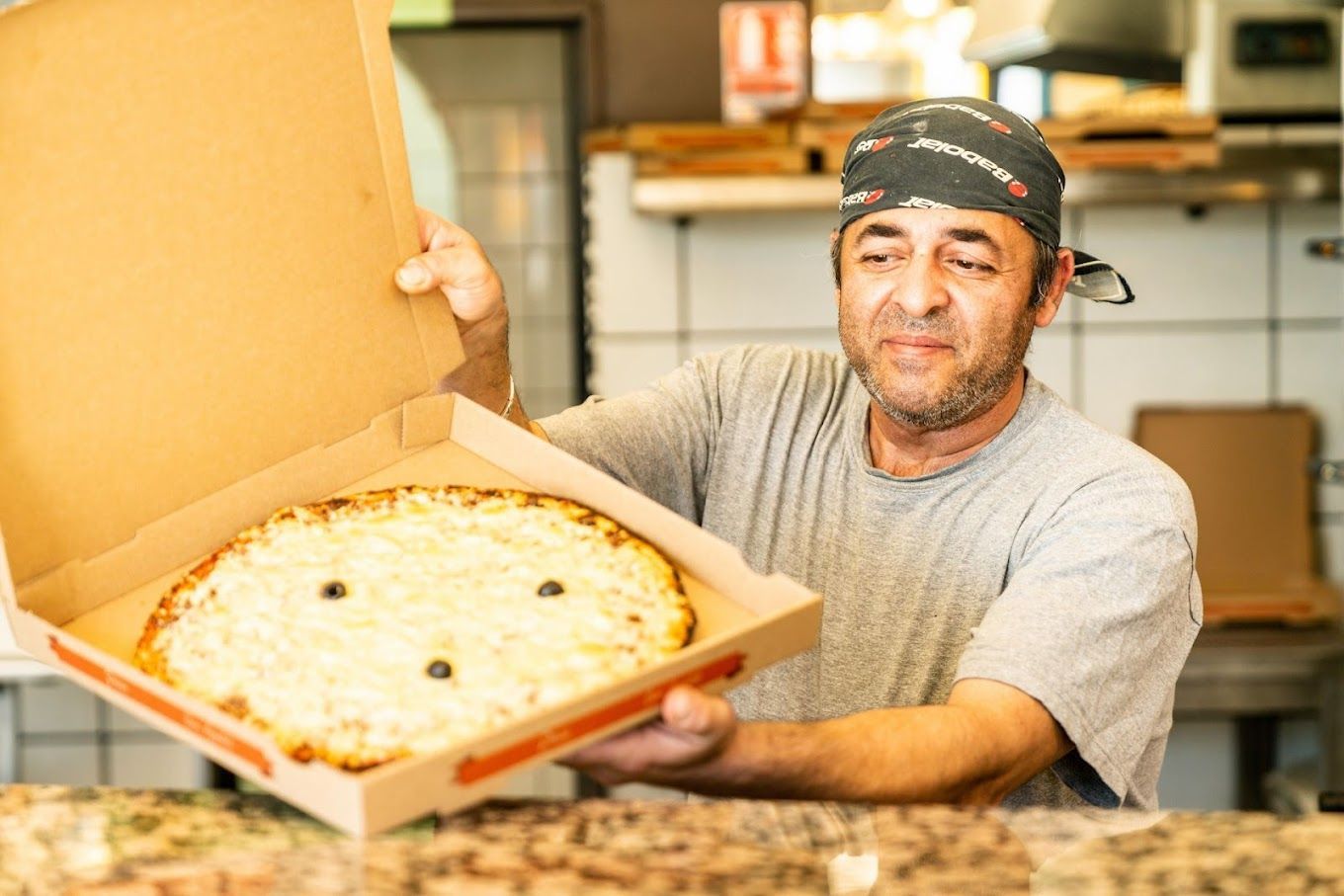 Photo d'un pizzaïolo tenant un carton de pizza avec une pizza à l'intérieur