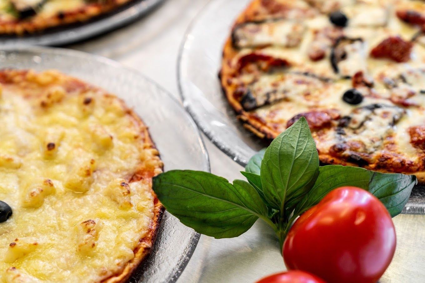 Photo de deux pizzas alignées et de tomates en bas des assiettes