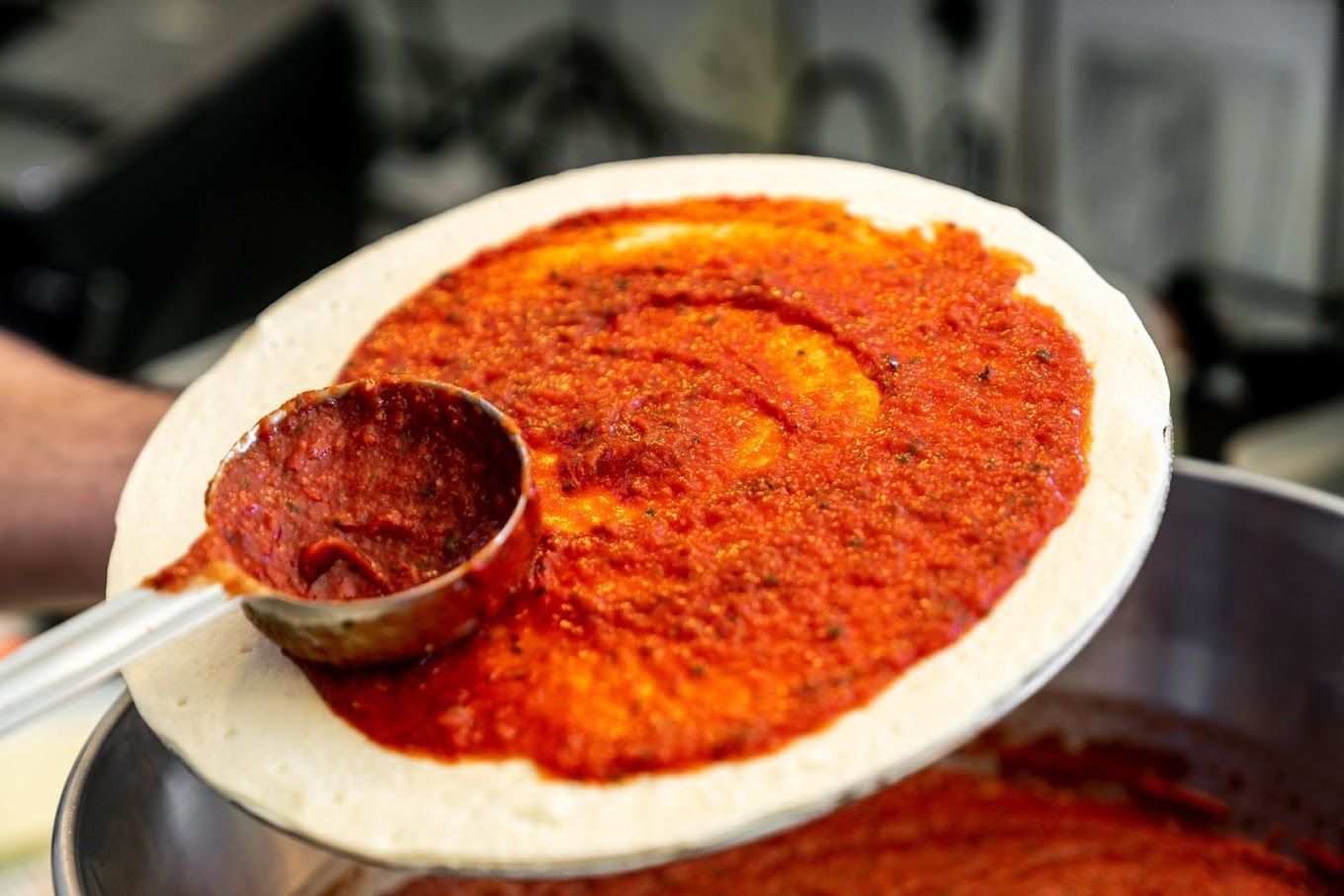 Photo d'une pâte à pizza en train d'être badigeonnée de sauce tomate
