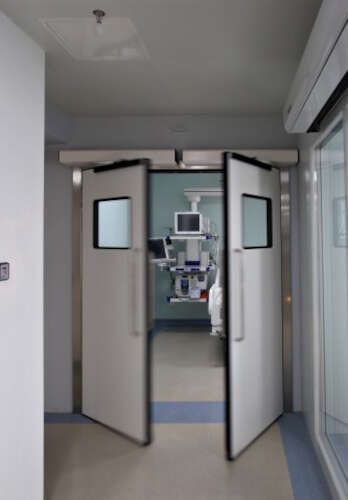 Un quirófano de hospital con dos puertas abiertas y un monitor colgando del techo.