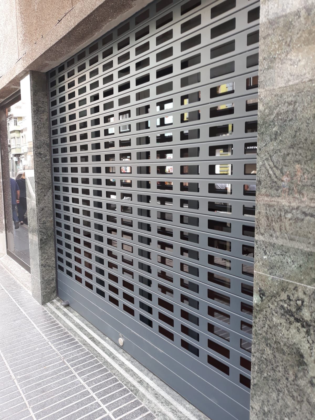 Una puerta de garaje gris con agujeros está en el costado de un edificio.