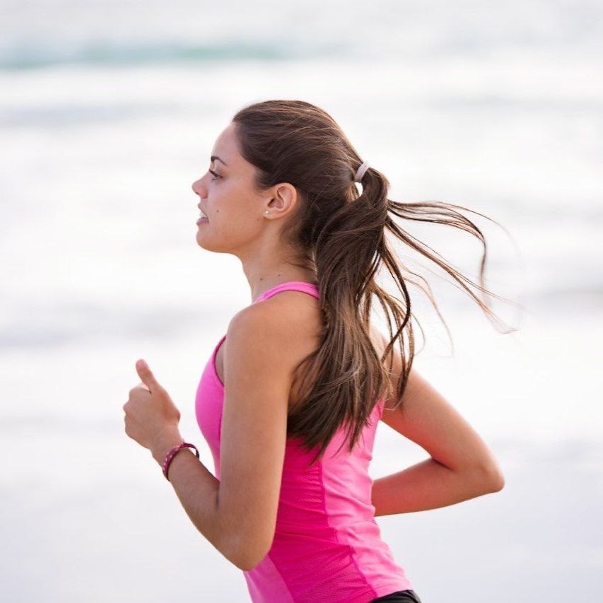 Una mujer con una camiseta rosa corre por la playa