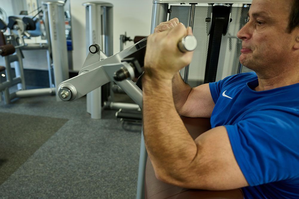Ein Mann in einem blauen Hemd benutzt ein Gerät in einem Fitnessstudio.