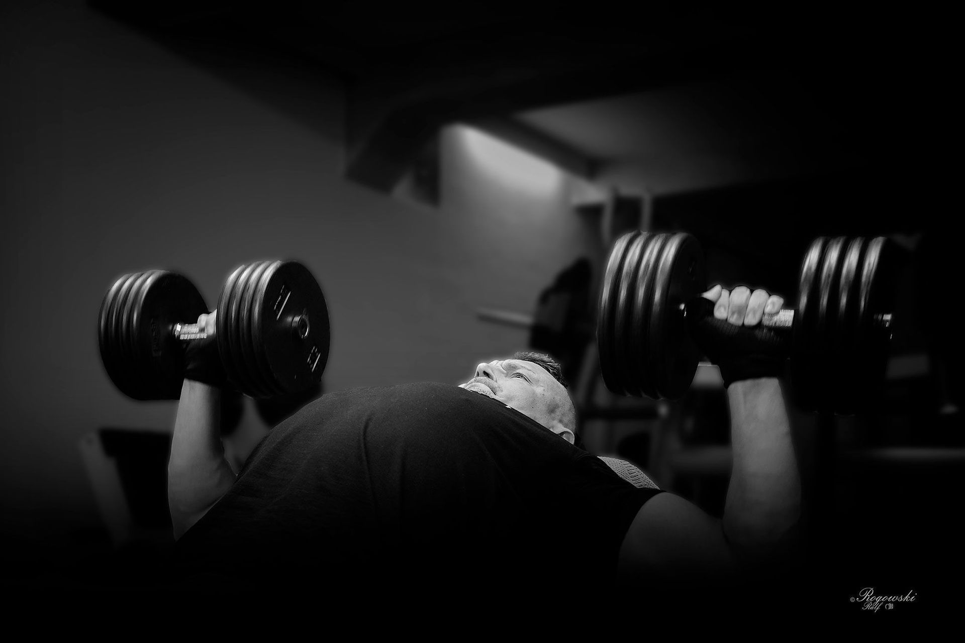 Ein Mann stemmt in einem Fitnessstudio Hanteln auf einer Bank.