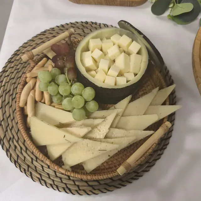 Una cesta de mimbre llena de queso en lonchas y uvas.