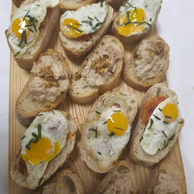 Un montón de sándwiches con huevos encima sobre una tabla de cortar de madera.